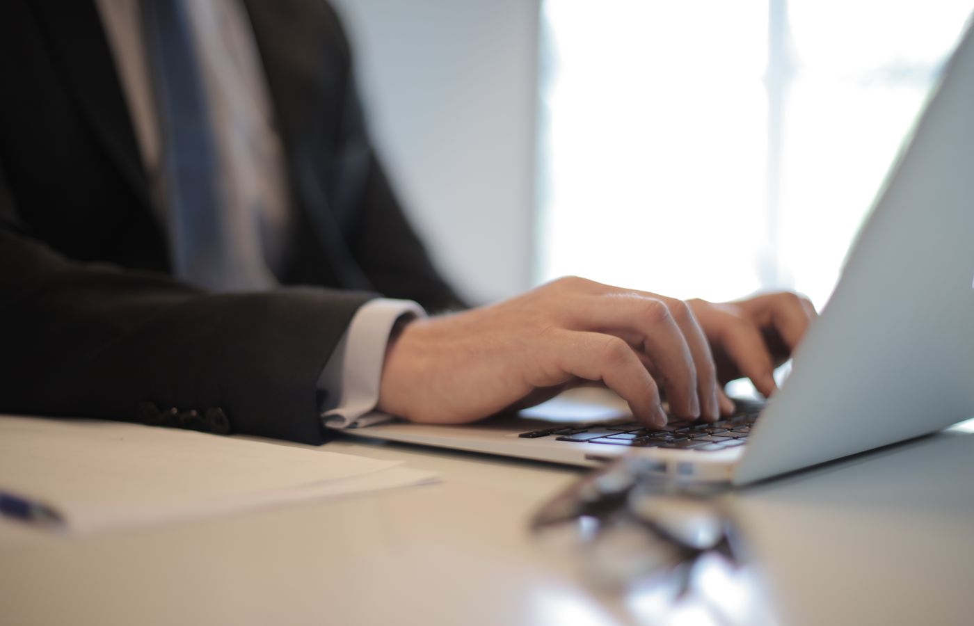 Close-up of businessman typing on a laptop in a modern office setting, showcasing remote work.