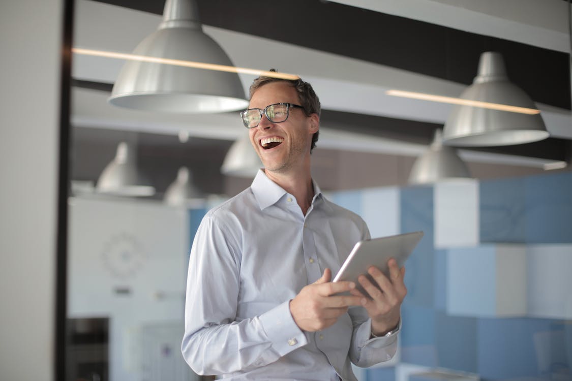 Free Photo of Laughing Man in White Dress Shirt Carrying a Tablet Stock Photo