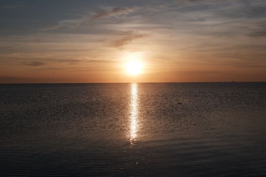 Calm ocean waters reflecting a serene sunset with golden skies, creating a peaceful scene.