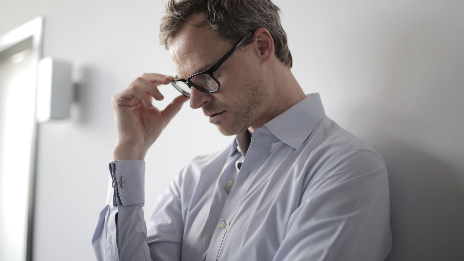Modafinil and Executive Function: Unlocking Your Cognitive Potential An adult man in a shirt and glasses appears stressed while leaning against a wall indoors.