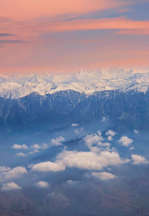 Free A breathtaking view of snow-capped mountains at sunrise, surrounded by clouds. Stock Photo