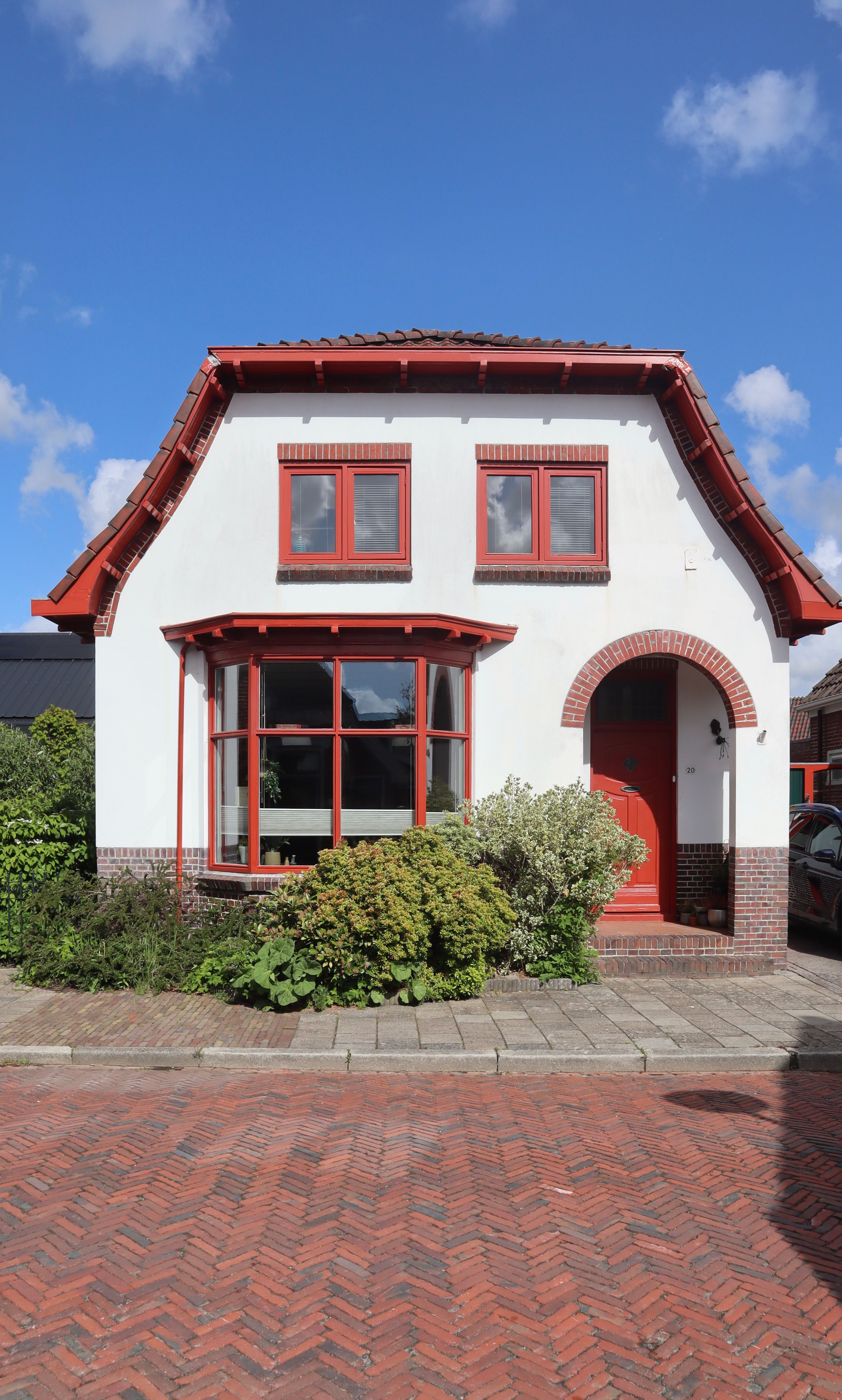 Charming traditional Dutch house with red accents in Winsum, Netherlands, set against a clear blue sky.