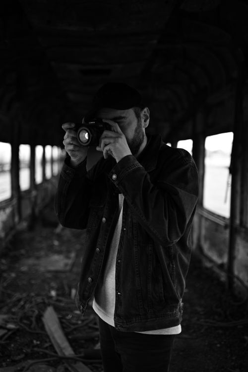 Free A man with a camera takes photos inside an old, abandoned train car, creating a moody and atmospheric scene. Stock Photo