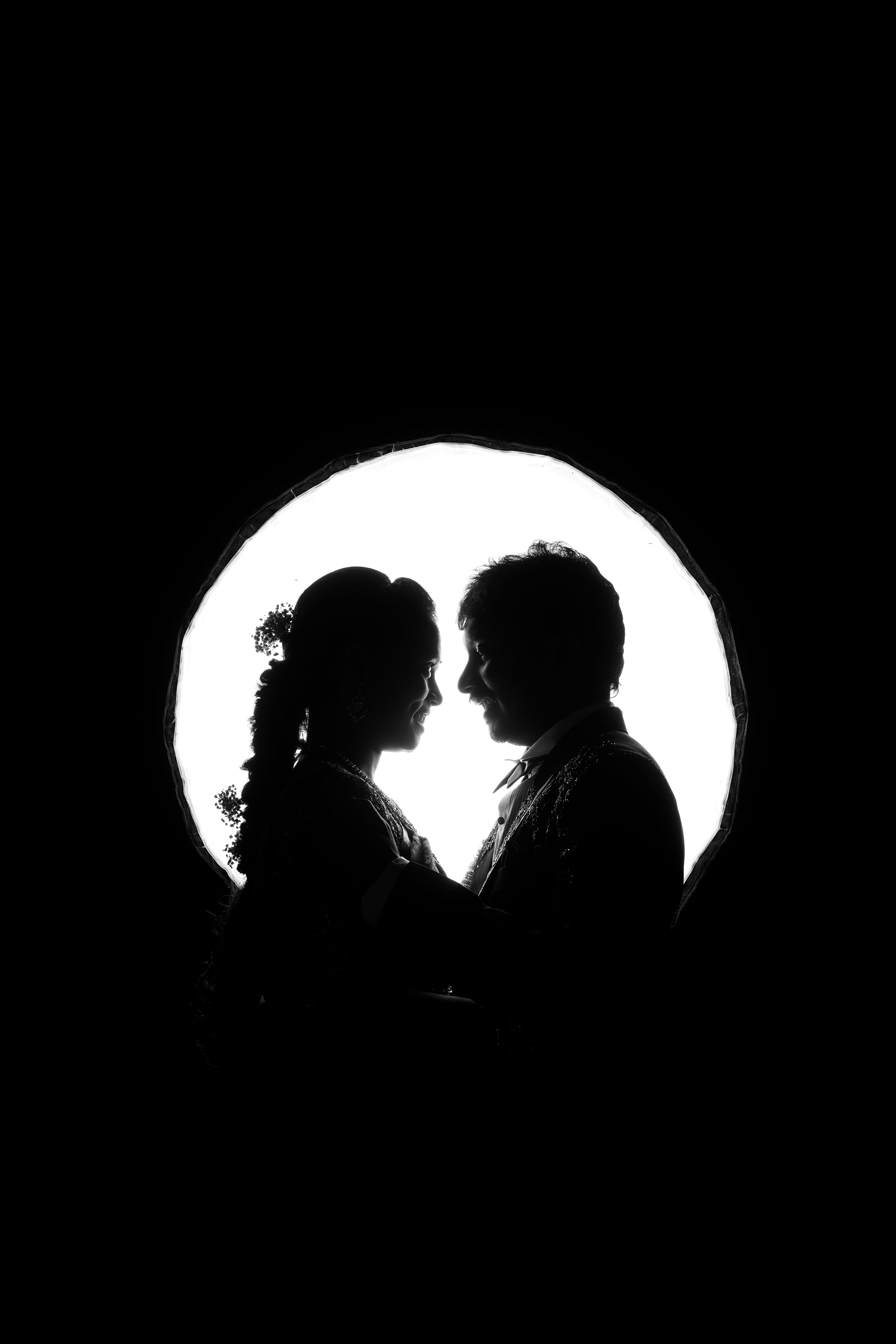 Silhouette of a South Asian couple sharing an intimate moment, framed by a bright circular background.