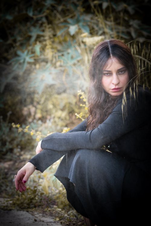 Free A mysterious woman crouches in a forest setting, conveying a moody and dramatic atmosphere. Stock Photo