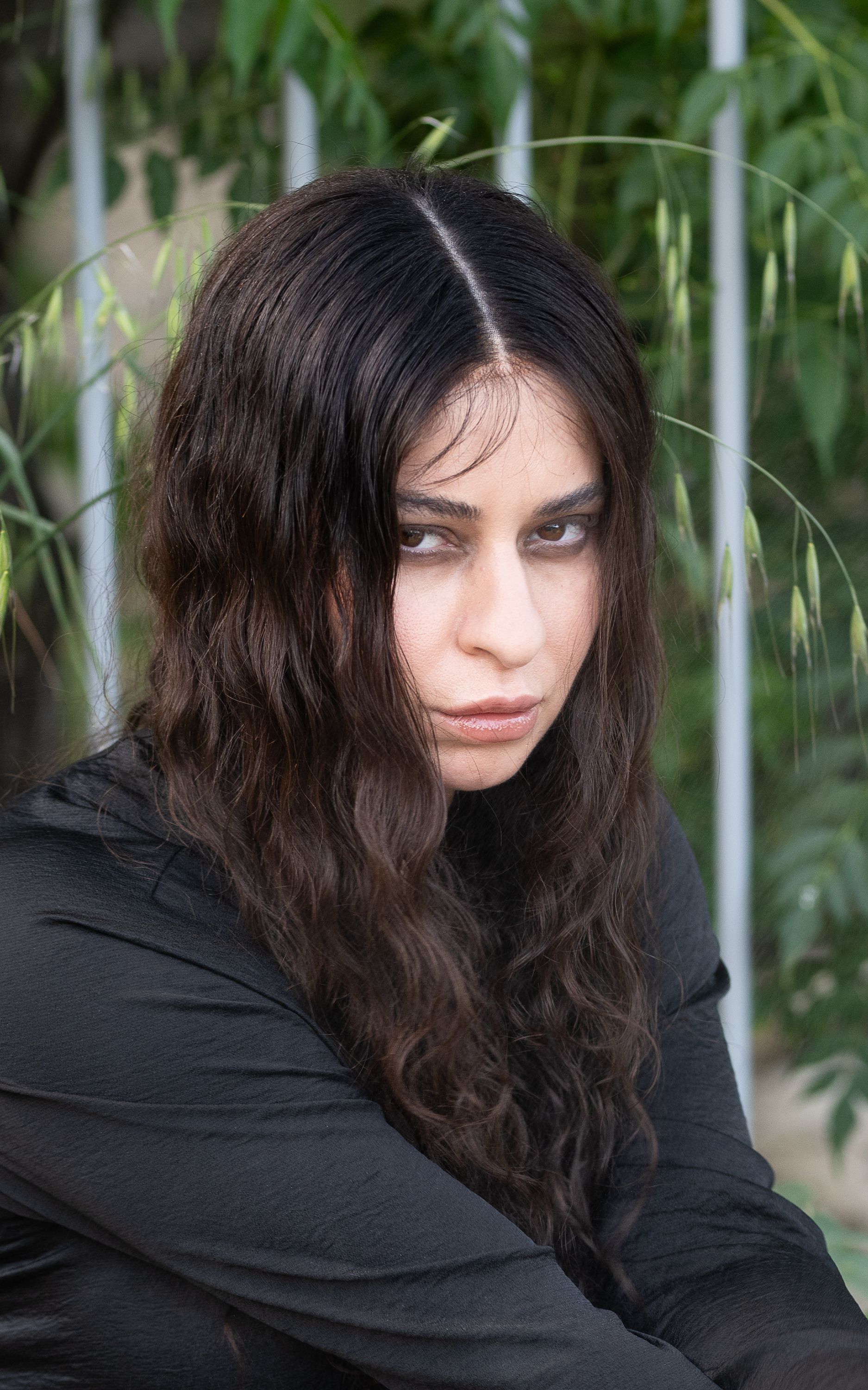 Close-up portrait of a woman in a black outfit with lush nature background, capturing a moody expression.