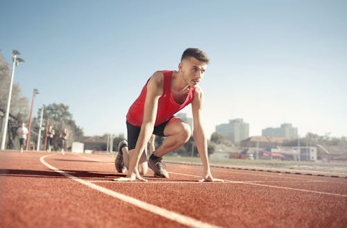 Free Man in Res Tank Top Running On Athletic Field Stock Photo