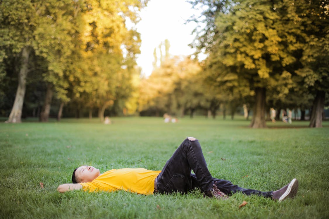 Free Photo of Man in Yellow T-shirt and Black Jeans Lying Down on Green Grass Field with Stock Photo