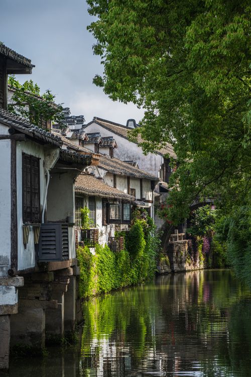 Free Picturesque canal view with traditional Chinese architecture in Suzhou. Lush greenery reflects on the calm water. Stock Photo