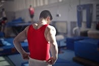Back view of muscular athlete in red uniform preparing for training in gymnast hall with equipment