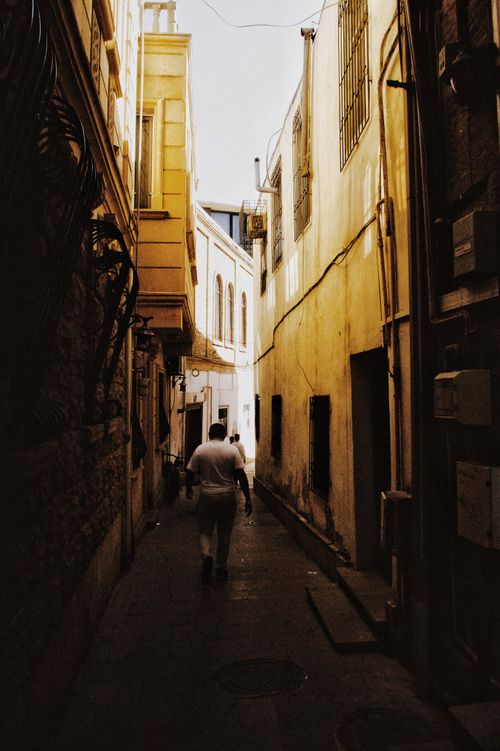 Free A solitary adult walking in a sunlit narrow alley in an urban setting. Stock Photo