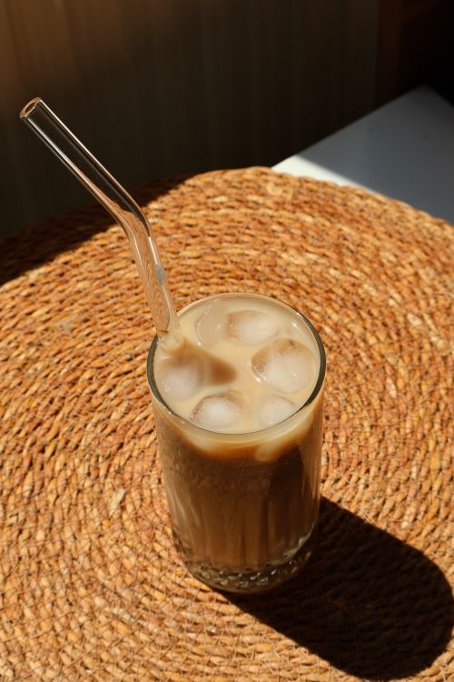 Free A glass of iced coffee with glass straw on a woven mat in warm sunlight. Stock Photo