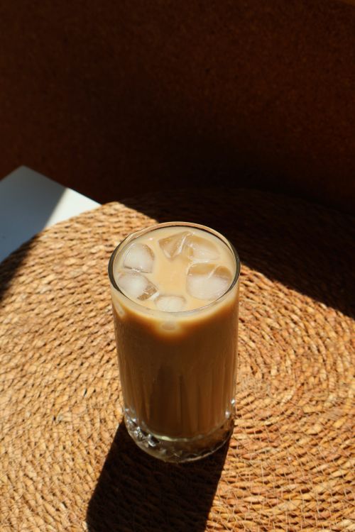 Free A glass of iced coffee with ice cubes sitting on a woven mat in sunlight. Stock Photo
