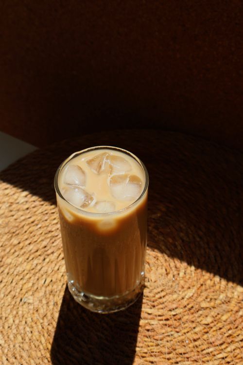 Free Glass of iced coffee on a woven mat, illuminated by sunlight against a dark background. Stock Photo
