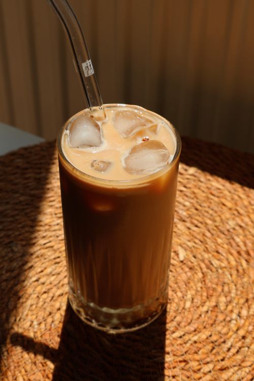 Free Chilled iced coffee served in a tall glass with ice cubes and straw on woven placemat. Stock Photo