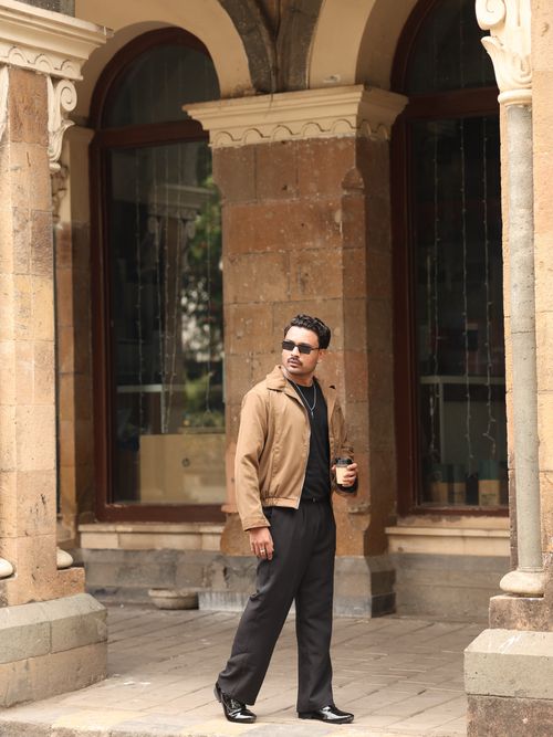 Free Man in fashionable attire holding coffee cup outside historic building with arches. Stock Photo