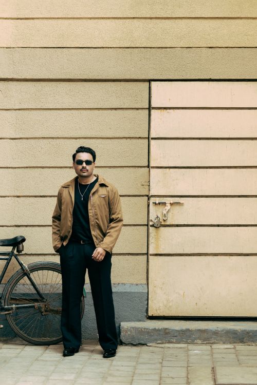 Free Man in casual attire leaning against a rustic wall beside a bicycle. Stock Photo