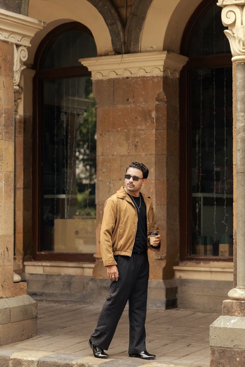 Free Casually dressed man in shades strolls by classical pillars on a city sidewalk, holding a drink. Stock Photo
