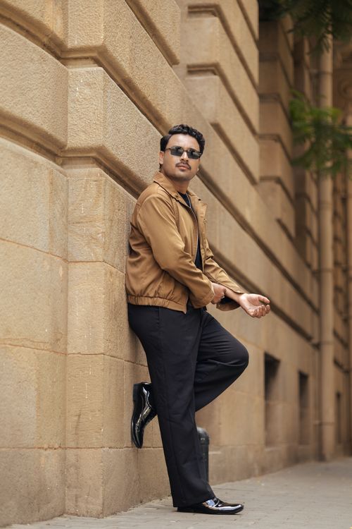 Free Stylish man in sunglasses leans against an urban building wall, exuding confidence and style. Stock Photo