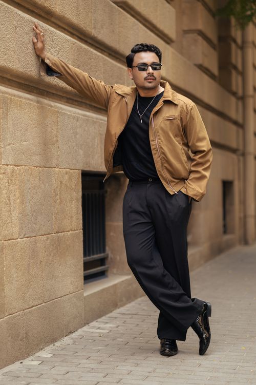 Free Fashionable man in casual outfit leans against a stone wall outdoors. Stock Photo
