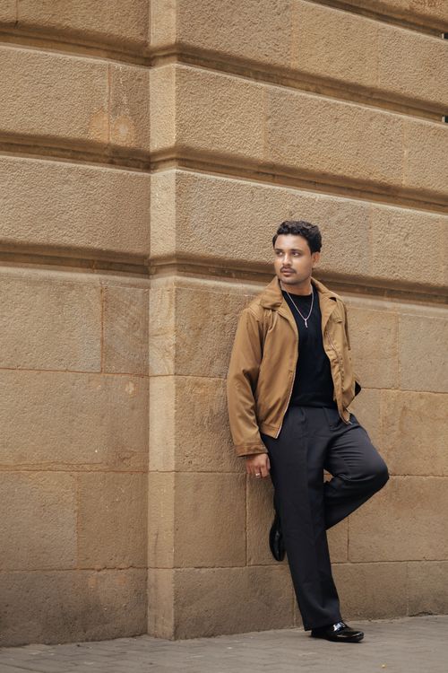 Free Fashionable adult man in casual attire leaning on a city building's stone wall. Stock Photo