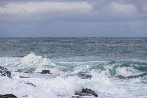 Free Dynamic ocean waves crashing against rocky shoreline under cloudy sky. Stock Photo