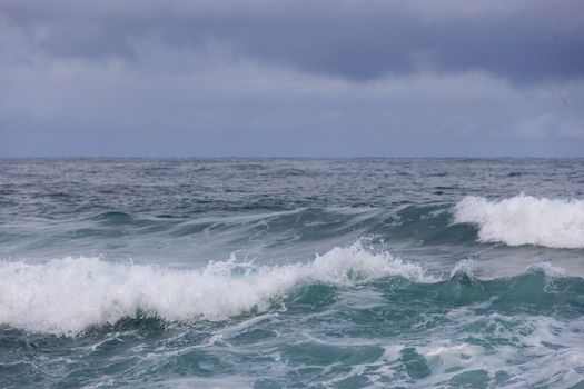 Powerful ocean waves crash beneath a moody, overcast sky, showcasing nature's raw energy.