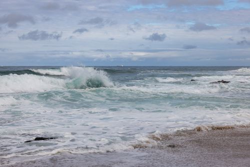 Free Capture of powerful ocean waves crashing against a rocky shore under a cloudy sky. Stock Photo