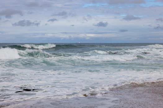 A serene coastal scene with waves crashing on the shore under a cloudy sky.