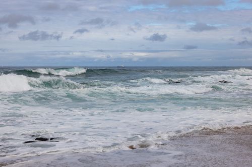 Free A serene coastal scene with waves crashing on the shore under a cloudy sky. Stock Photo