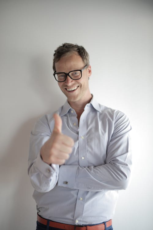 Photo of Smiling Man in Blue Dress Shirt and Black Framed Eyeglasses Giving Thumbs up