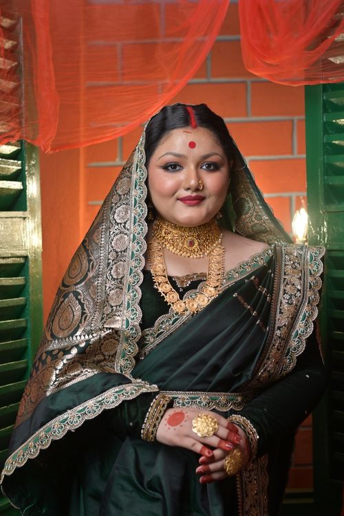 Free A traditional Indian bride in a green saree with intricate jewelry, standing indoors with elegant decor. Stock Photo