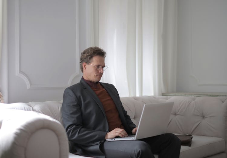 A Man Sitting On A White Couch Using Laptop