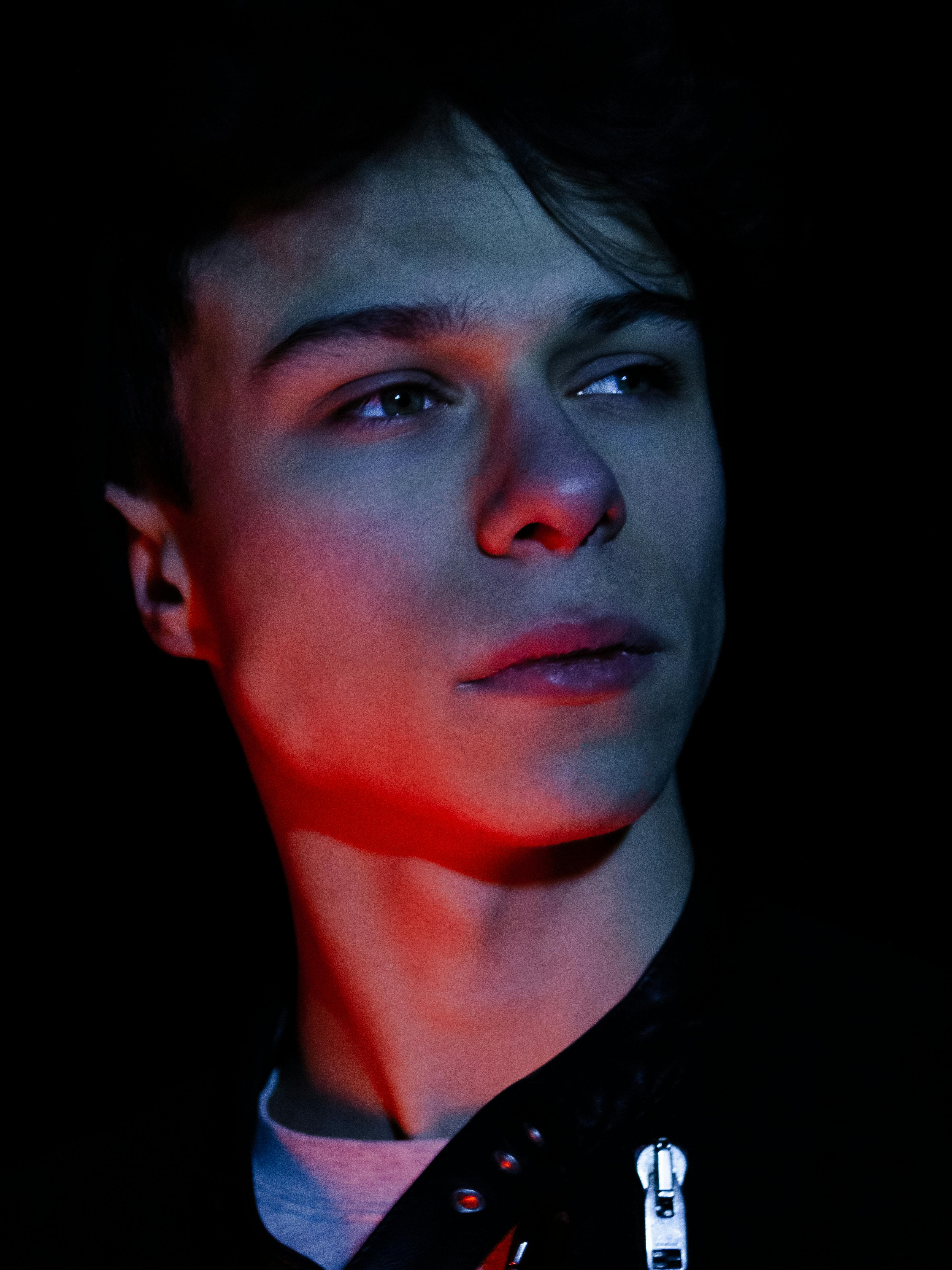 Dramatic portrait of a male model with red and blue lighting creating a striking effect.