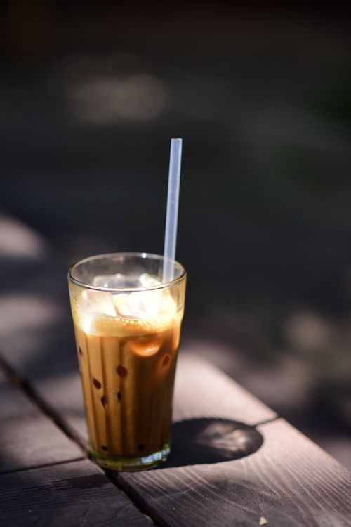 Free Close-up of an iced coffee with straw on a wooden table, captured in natural light. Stock Photo