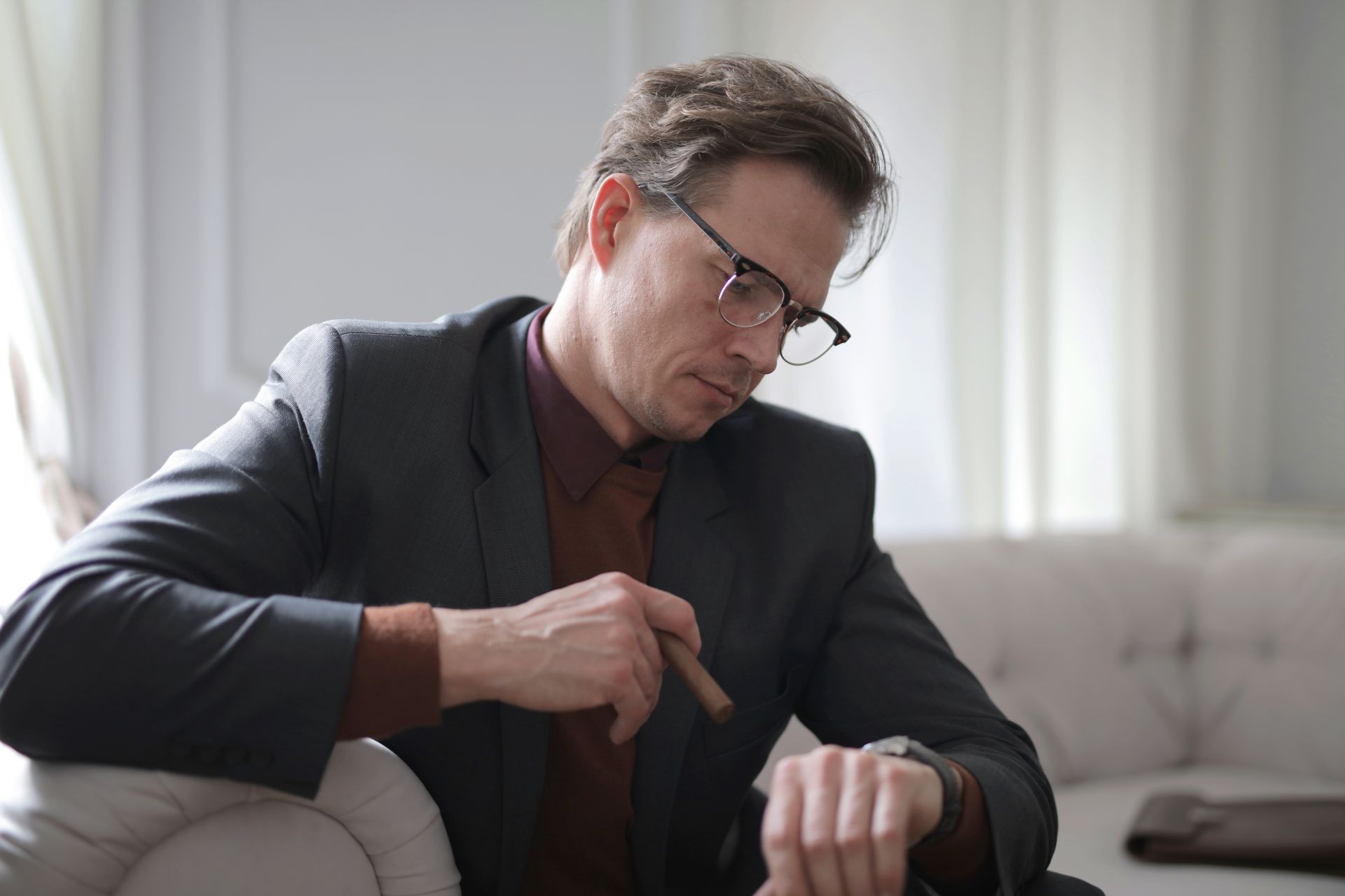 Man in a suit, checking time on wristwatch while holding a cigar indoors.