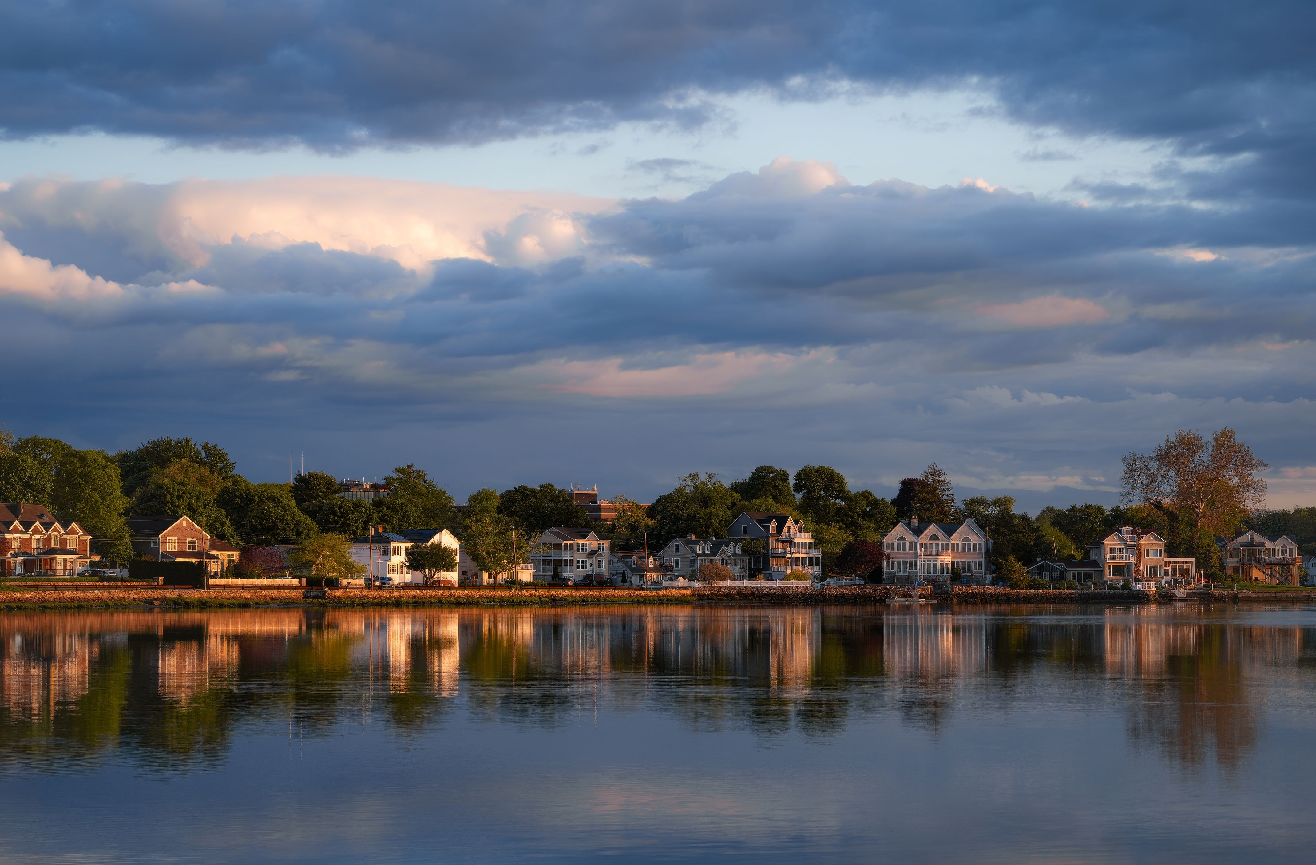 Charming suburban homes reflected in a calm lake under a dramatic twilight sky.