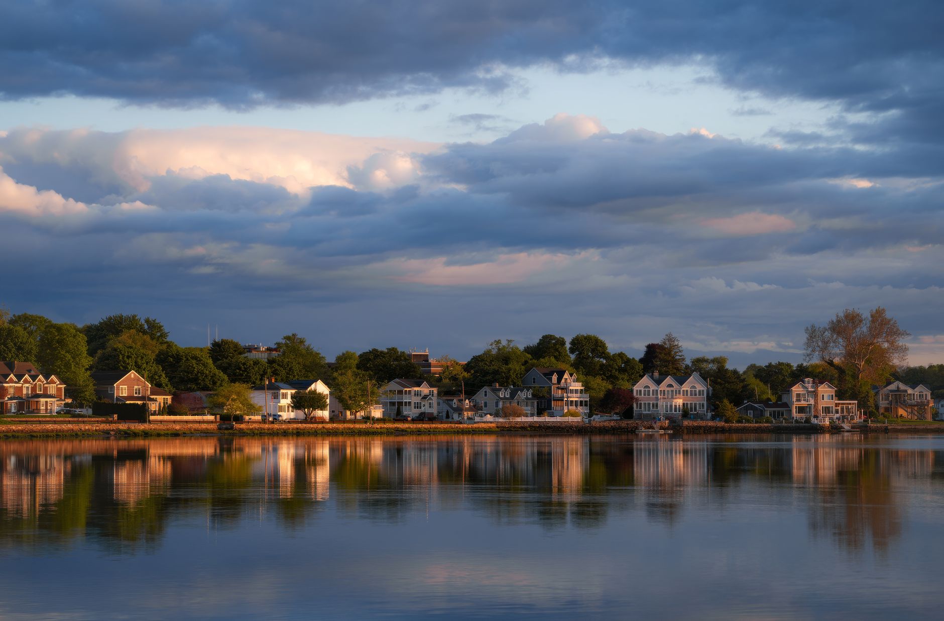 Charming suburban homes reflected in a calm lake under a dramatic twilight sky.