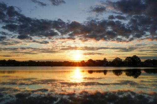 Free Breathtaking sunset with colorful clouds reflecting over a serene lake, creating a peaceful scene. Stock Photo