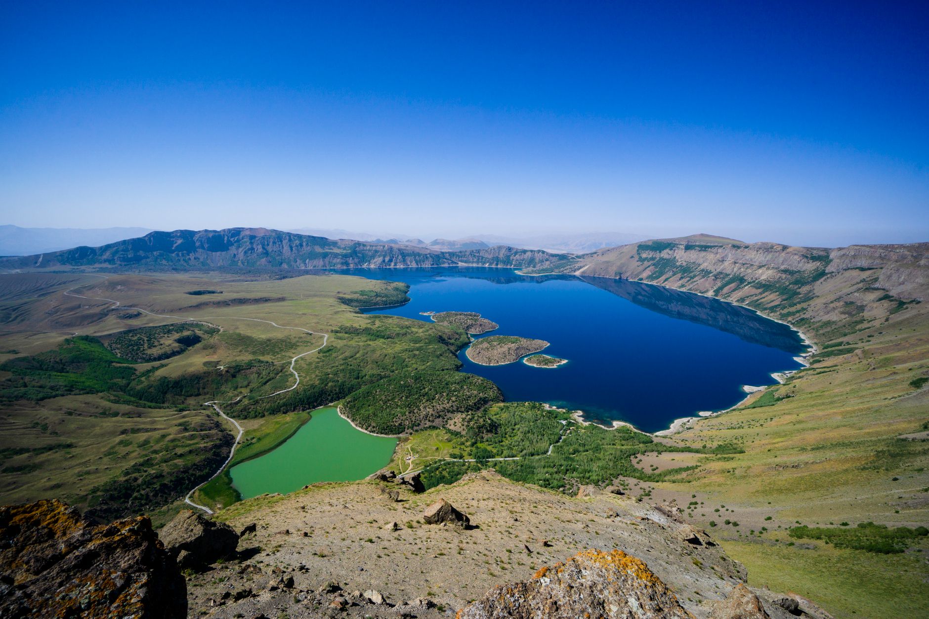 Breathtaking aerial shot of vibrant crater lakes surrounded by rugged terrain under a clear blue sky.