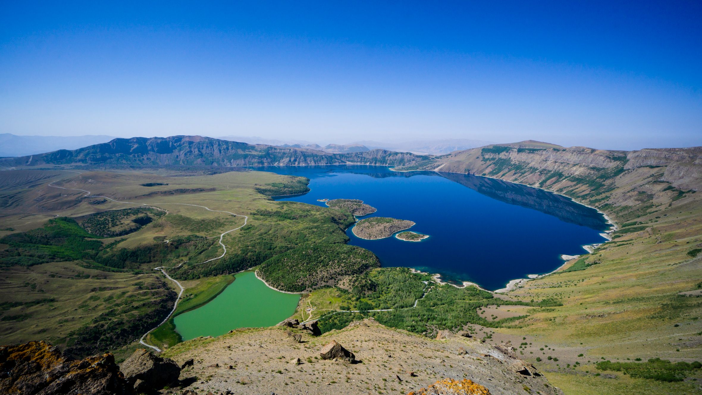 Breathtaking aerial shot of vibrant crater lakes surrounded by rugged terrain under a clear blue sky.