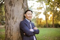 一个穿着正式服装的自信男人微笑着靠在户外的树上