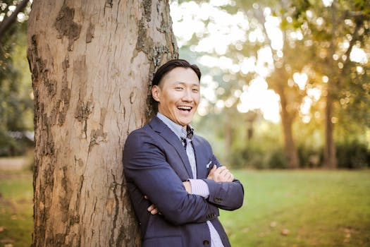 在公园里，一位微笑的亚洲男子穿着西装靠在一棵树上，享受着明媚的一天