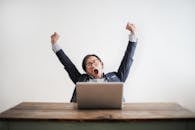 Photo of Yawning Man with His Hands Up and Eyes Closed Sitting at a Table with His Laptop