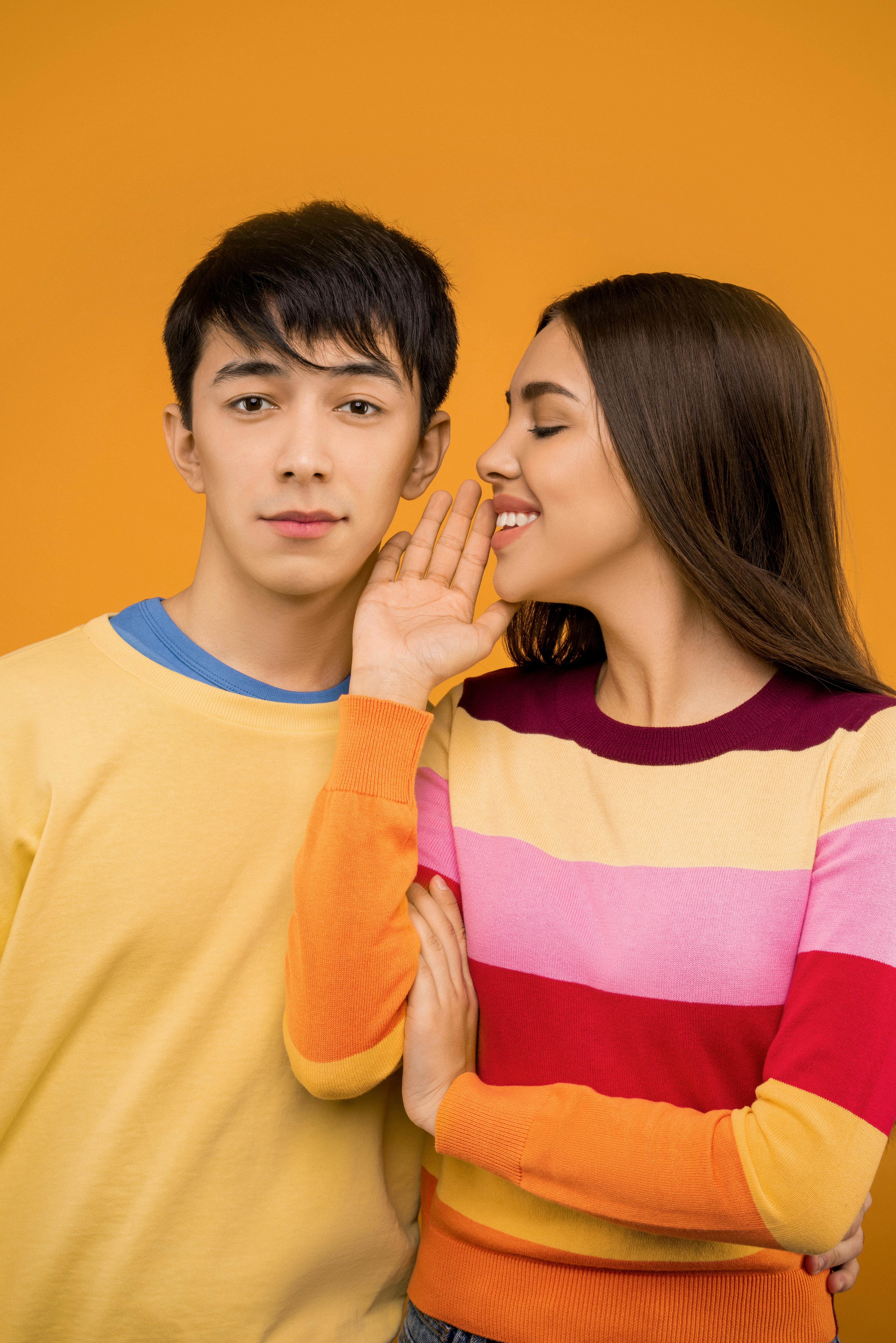 一对幸福的情侣穿着五颜六色的毛衣，在充满活力的橙色背景下相拥