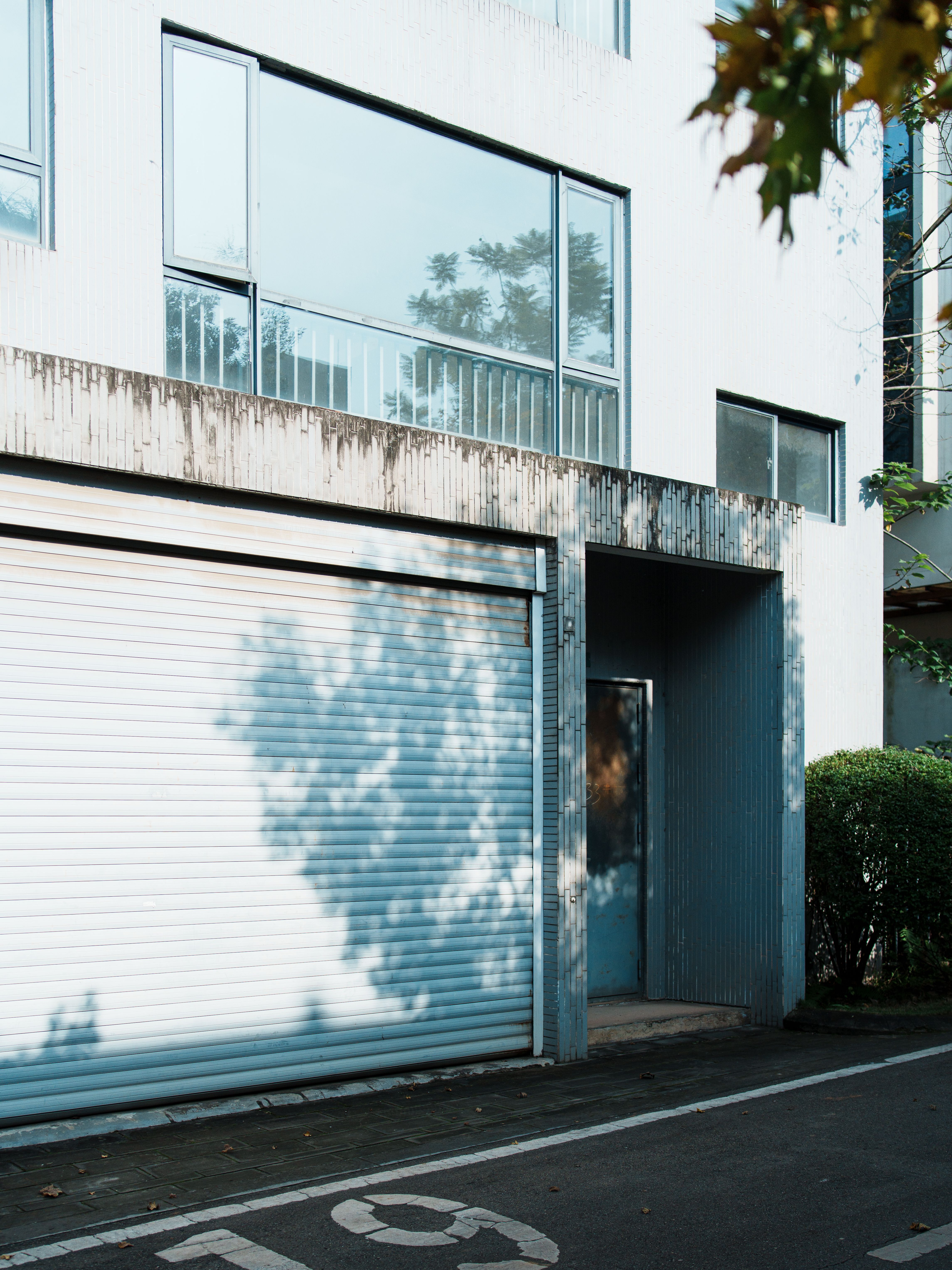Minimalist architectural style of a building in Chengdu, featuring a white garage door and leafy shadows.