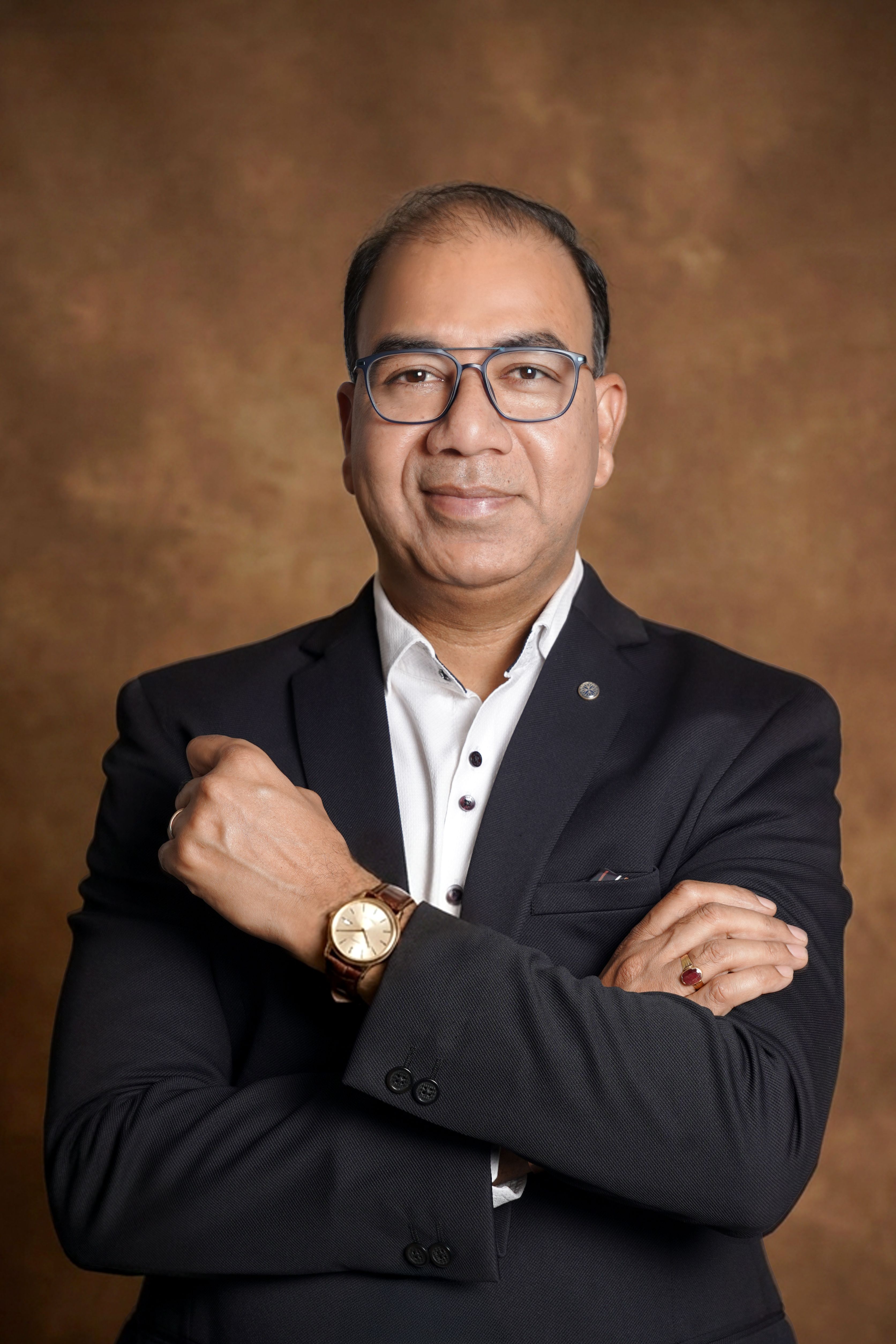 Portrait of a confident businessman in a suit with glasses and a watch against a brown background.