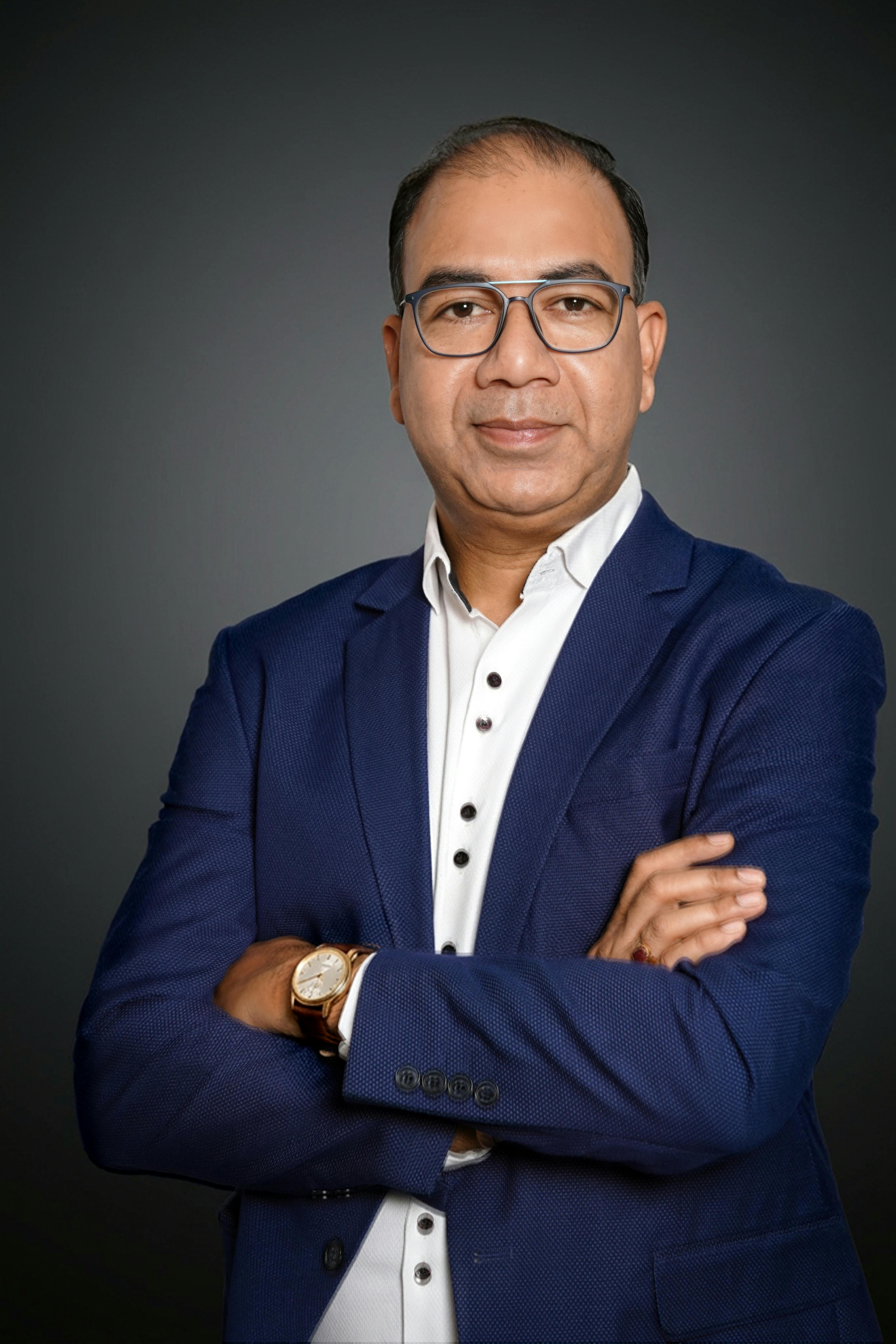 Professional portrait of a confident businessman wearing glasses in a blue suit.