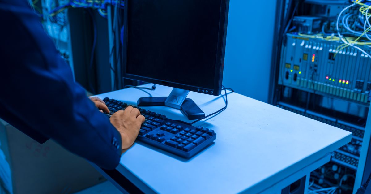 An IT professional operates a computer in a server room, managing network systems and connected devices.
