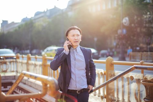 Free Confident Asian man in business attire making a phone call outdoors on a sunny day. Stock Photo